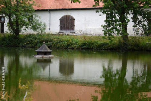 wooden house for ducks on a lake in front of a historic building, refelctions in the water photo