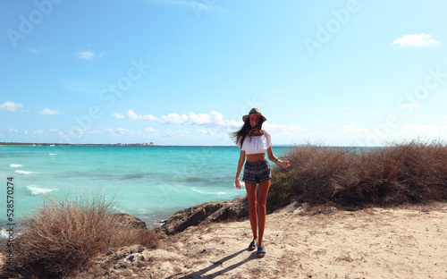 Attractive brunette with curly hair woman. Cute charming girl walks in Spain, Mallorca. Chill and comfort. Beautiful girl in a white shirt looks at the sea. Marine background. Relaxed atmosphere.