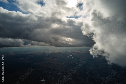 Aerial view from airplane window at high altitude of distant city covered with white puffy cumulus clouds