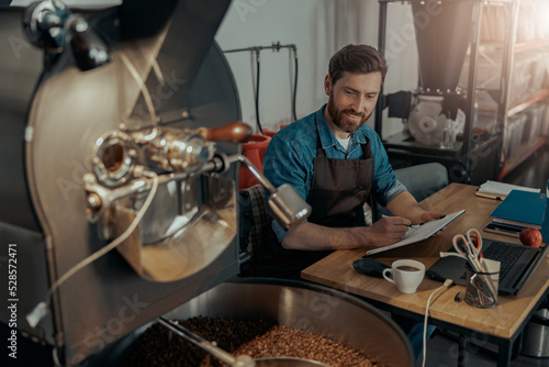 Warehouse worker of small coffee roasting factory working on workplace with documents