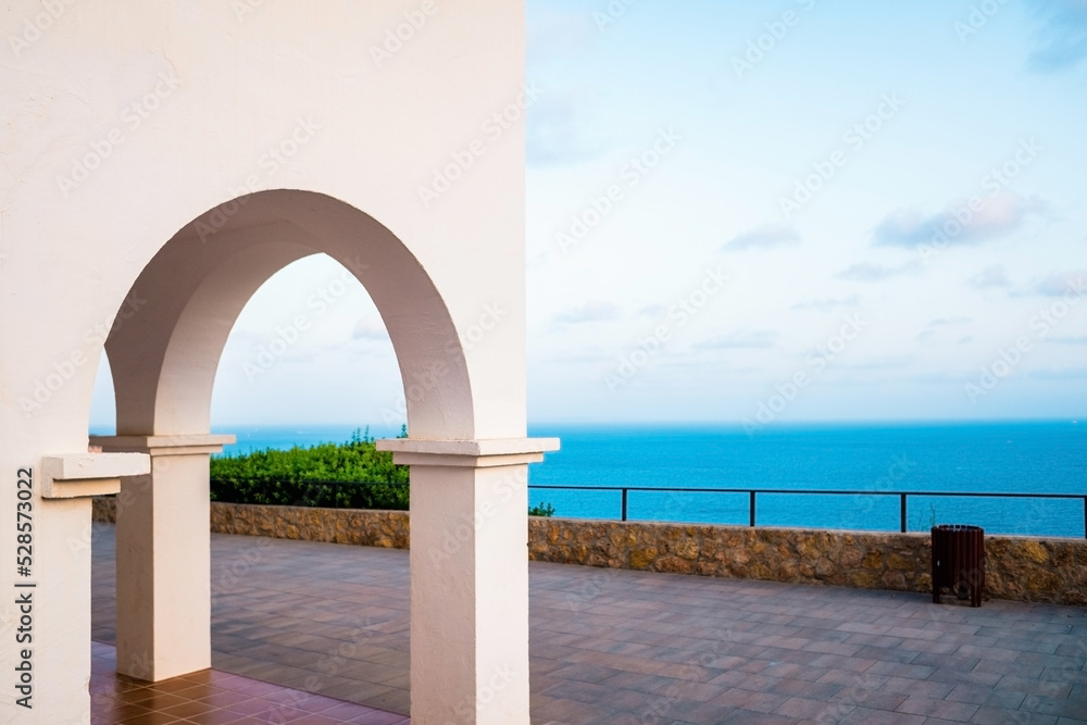 The sea can be seen from the top of a hill, through the traditional white arches of the Mediterranean houses.
