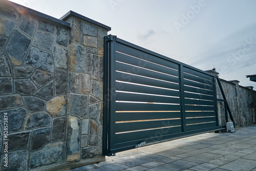Fototapeta Wide automatic sliding gate with remote control installed in high stone fense wall