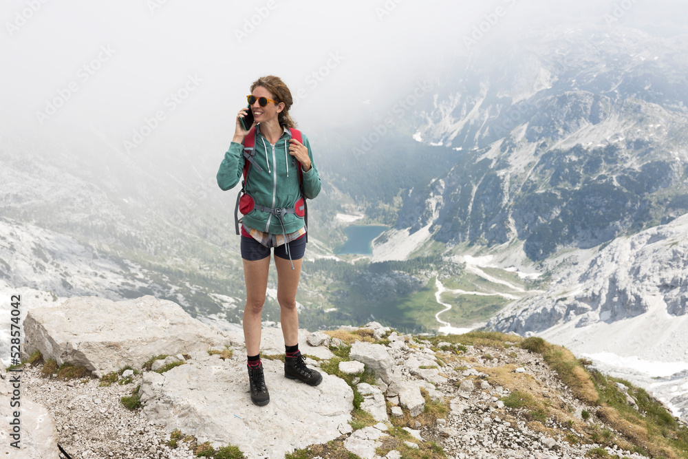Female Mid Adult Hiker Talking on a Mobile Phone from Top of a Mountain In European Alps - Krn Mountain Julian Alps Slovenia