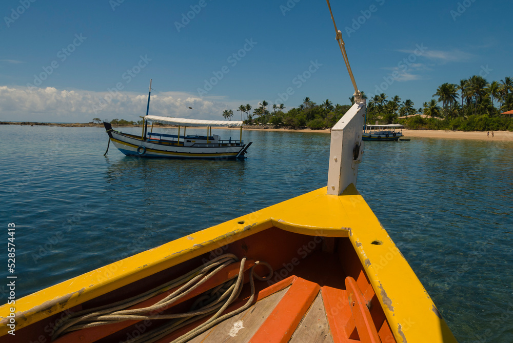 Bow of a yellow wooden boat near the beach in the village of Morro de São Paulo, Bahia, Brazil on a sunny day.
