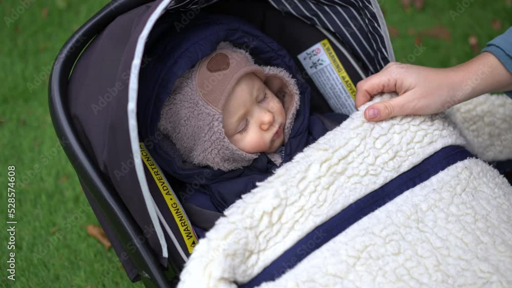 Zoom in to charming sleeping infant in baby stroller with female hands covering child with