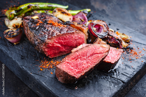 Barbecue dry aged wagyu roast beef steak with BBQ chili and onion rings served as close-up on a charred black wooden board photo