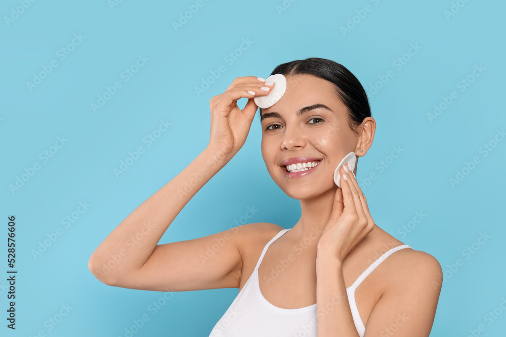 Young woman using cotton pads with micellar water on light blue background Young woman using cotton pads with micellar water on light blue background