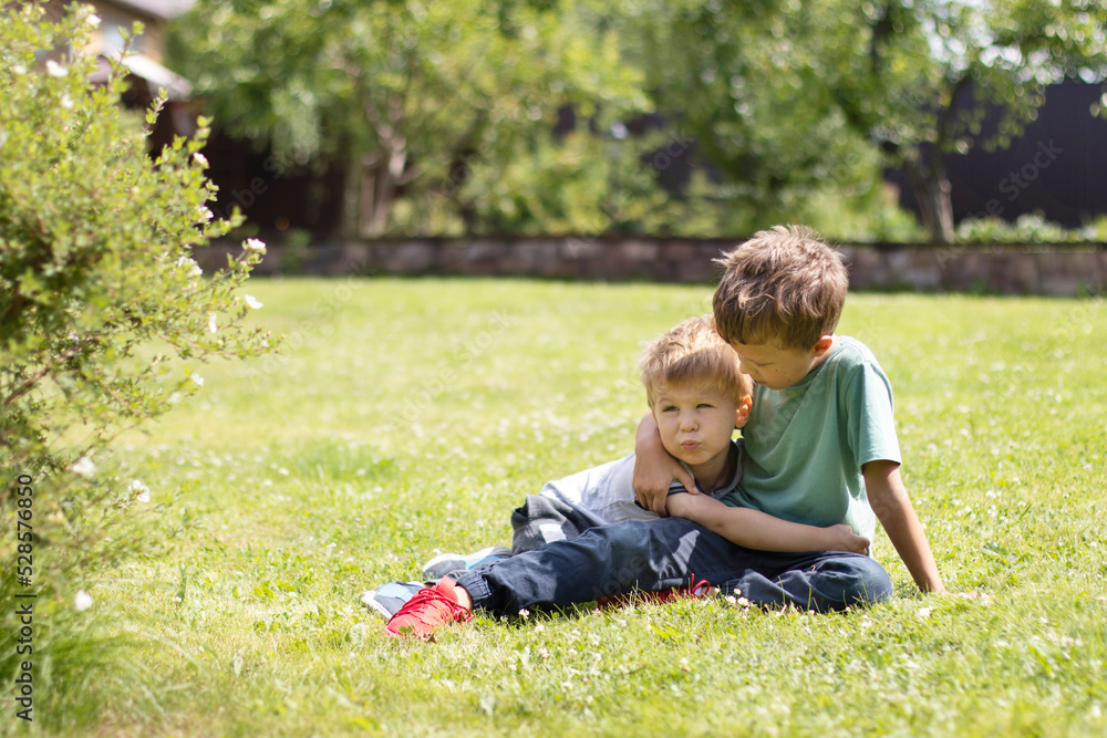 Two little brother boys lie on the grass and hug. Family ties and friendship concept