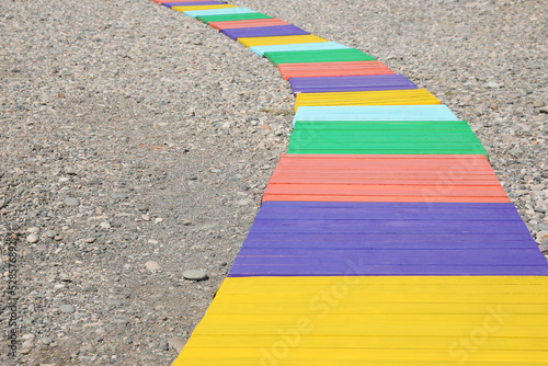 Colorful wooden walkway on pebble beach. Space for text