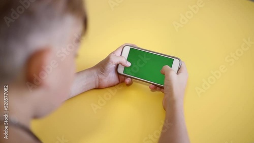 green screen. The child is holding a Smartphone in hand Close-up playing a game. phone with blank green screen mock up display for advertising. Slow motion.