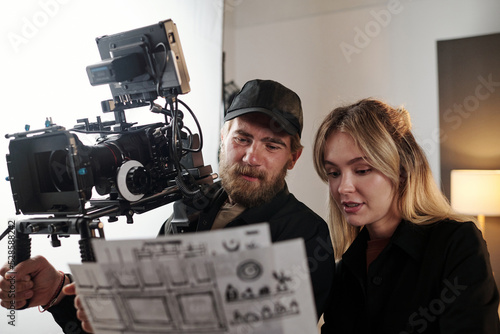 Valokuva Bearded videographer with videocamers and his blond female assistant discussing