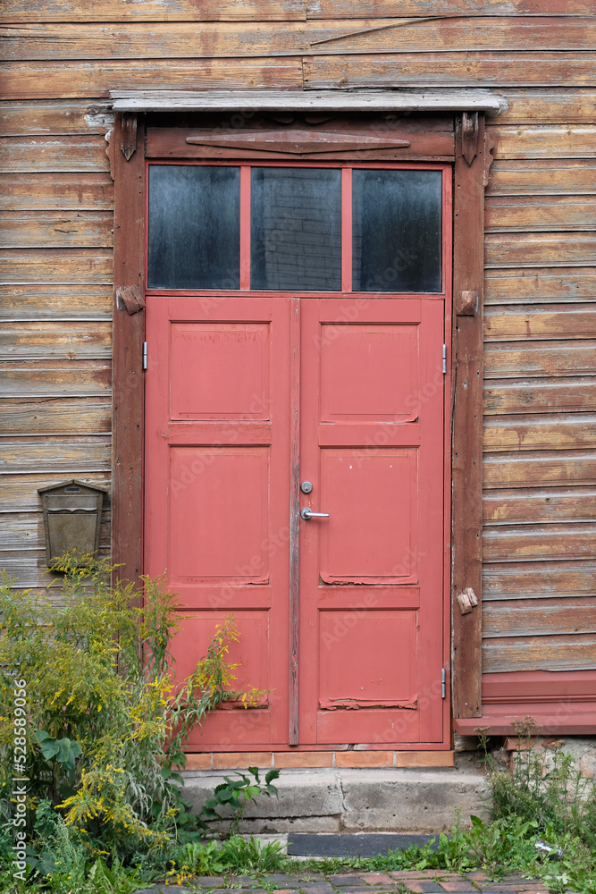 Old red wooden doors, entrance to wooden house with withered peeling paint on the walls. Tartu, Estonia. European historic architectural details. Old red wooden doors, entrance to wooden house with withered peeling paint on the walls. Tartu, Estonia. European historic architectural details.