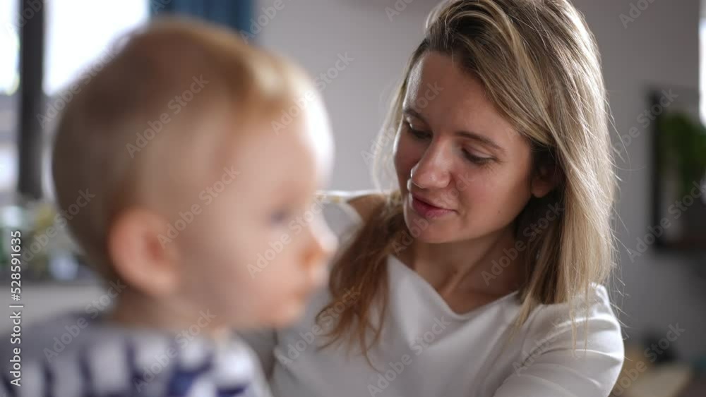 Close-up portrait of happy woman feeding infant talking and smiling. Beautiful Caucasian mother taking care of little daughter in kitchen at home indoors. Lifestyle and motherhood concept Close-up portrait of happy woman feeding infant talking and smiling. Beautiful Caucasian mother taking care of little daughter in kitchen at home indoors. Lifestyle and motherhood concept