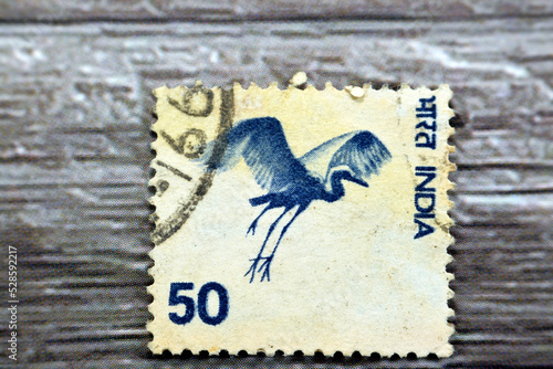 Old used Indian postage stamp printed in India 1975 50p from the country motifs series features gliding bird Virgin Crane (Anthropoides virgo) isolated on wood background photo