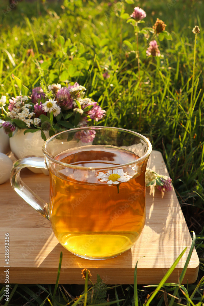 Cup of aromatic herbal tea, pestle and ceramic mortar with different wildflowers on wooden board in meadow Cup of aromatic herbal tea, pestle and ceramic mortar with different wildflowers on wooden board in meadow