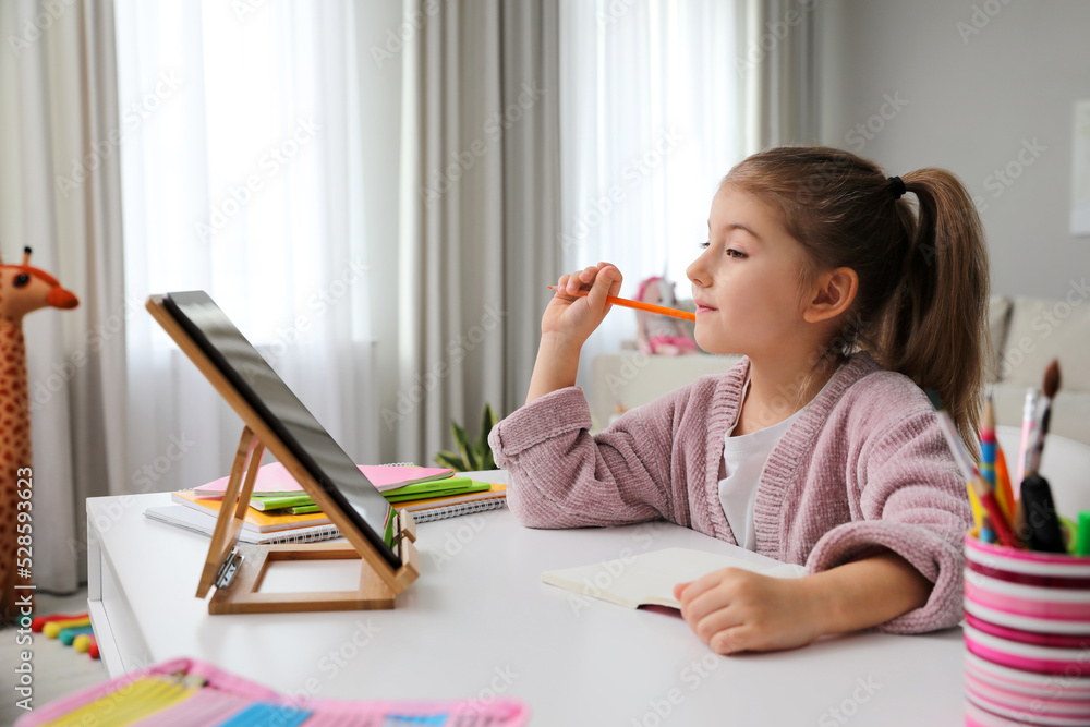 Adorable little girl doing homework with tablet at table indoors Adorable little girl doing homework with tablet at table indoors