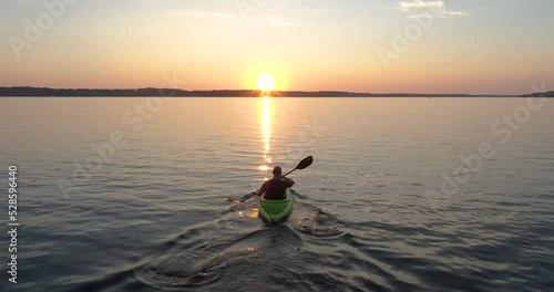 Person kayaking on lake paddling into the sunset.   photo