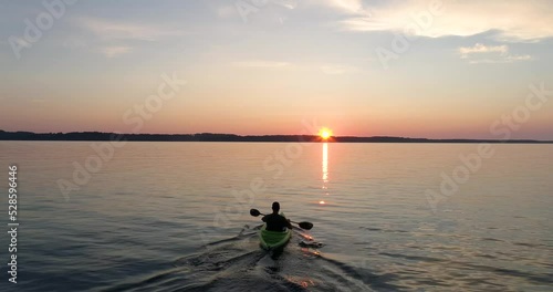 Person kayaking on lake paddling toward sunset on the horizon.  photo