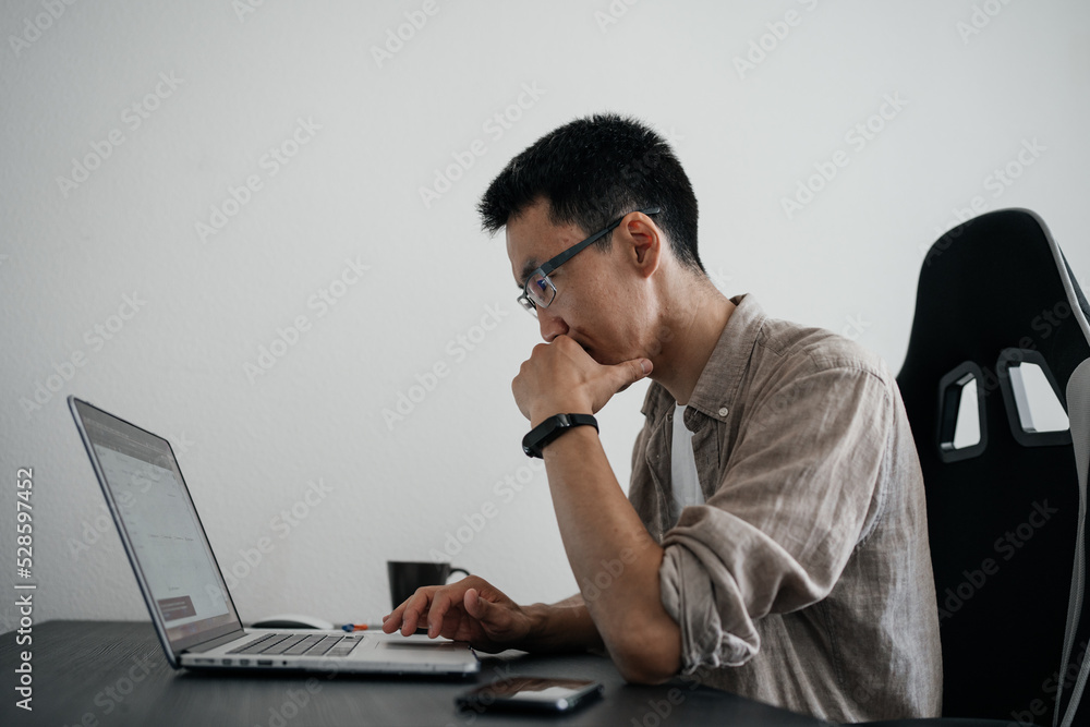 Middle aged asian man working at home with laptop.
