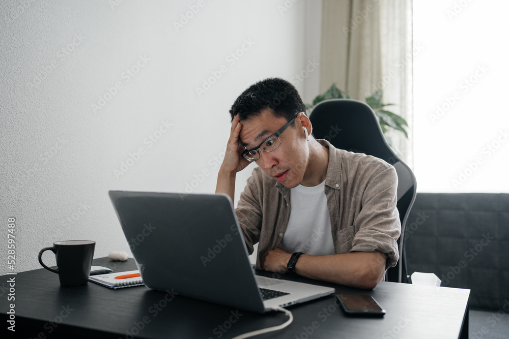 Middle aged surprised asian man working at home with laptop. Middle aged surprised asian man working at home with laptop.