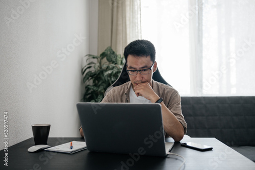 Middle aged asian man working at home with laptop.