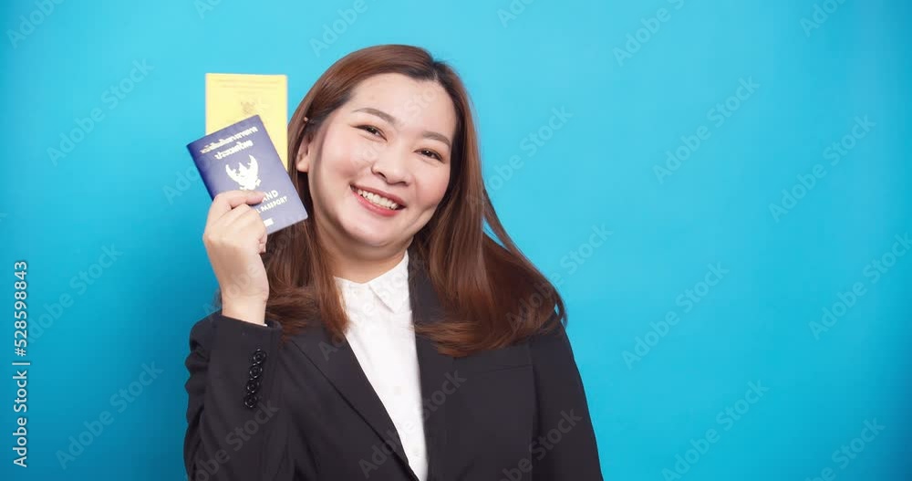 Asian businesswoman happy in suit and hand holding passport and vaccination card isolated on blue background Asian businesswoman happy in suit and hand holding passport and vaccination card isolated on blue background