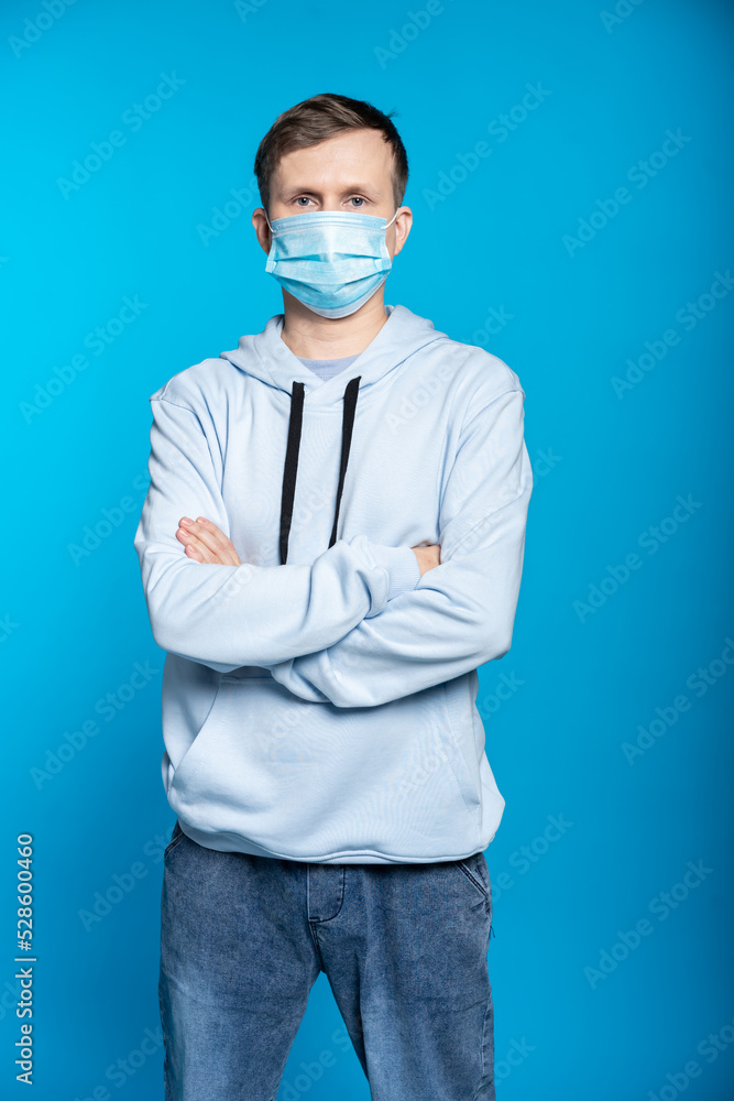 a guy in a blue sweatshirt, jeans put on a mask on his face and crossed his arms over his chest. blue background a guy in a blue sweatshirt, jeans put on a mask on his face and crossed his arms over his chest. blue background