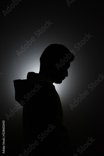 Cleanly define silhouette of man looking down wearing hood