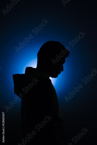 Cleanly define silhouette of man looking down wearing hood blue background