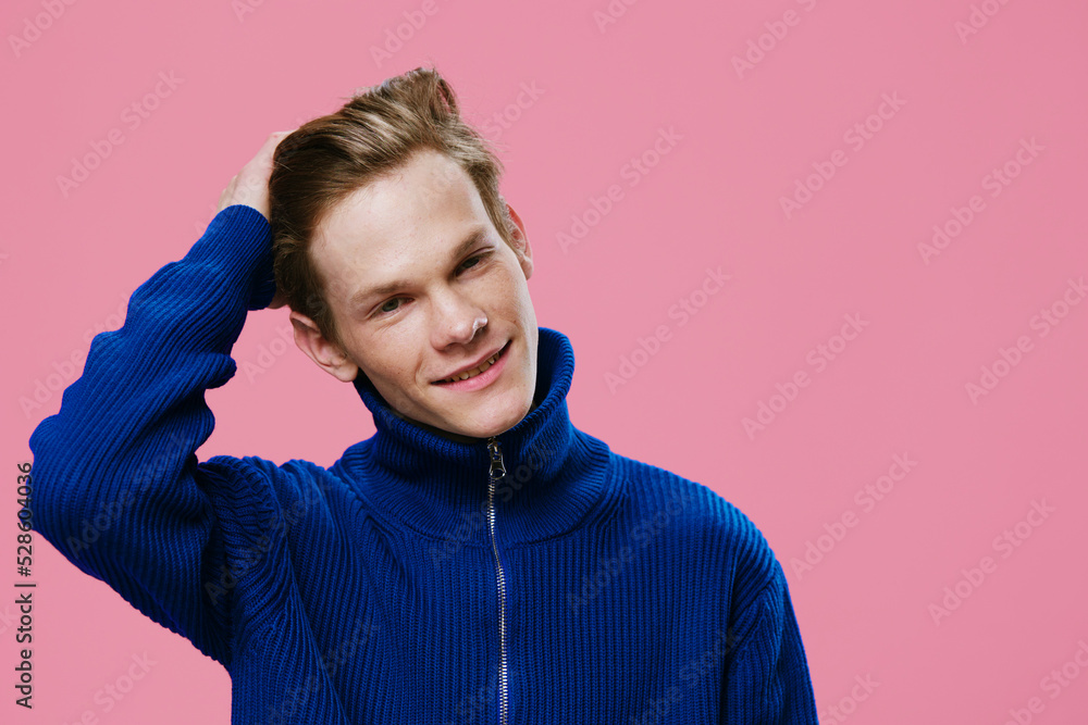 portrait of a cute, handsome guy with long hair in a blue sweater, holding his head with his hand while straightening his hair while standing on a pink background portrait of a cute, handsome guy with long hair in a blue sweater, holding his head with his hand while straightening his hair while standing on a pink background