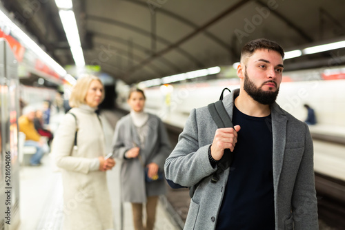 Portrait of young bearded man waiting for train in crowded subway station..