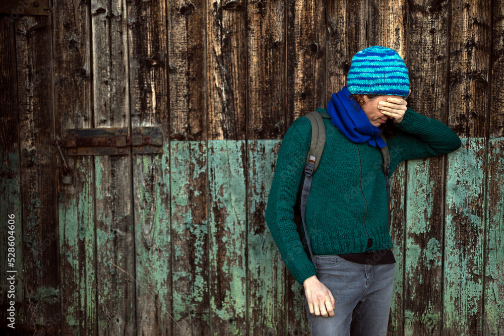 Casual Dressed Mid Adult Woman in Front of a Wooden Vintage Door Trying to Hide Her face with a Hand