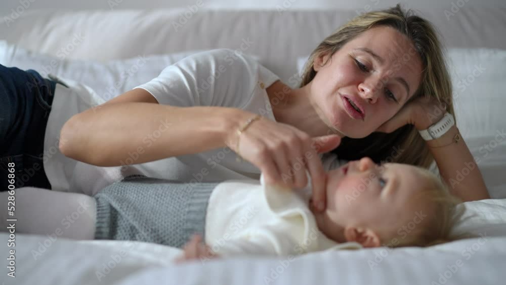 Portrait of loving mother lying on bed with blurred baby girl talking caressing face of curios kid. Happy confident Caucasian woman enjoying tranquility with toddler daughter in bedroom indoors Portrait of loving mother lying on bed with blurred baby girl talking caressing face of curios kid. Happy confident Caucasian woman enjoying tranquility with toddler daughter in bedroom indoors