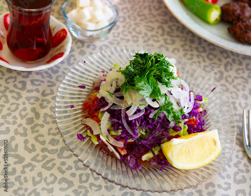 Colorful refreshing salad from chopped red cabbages, cucumbers, tomatoes and onion garnished with fragrant greens and lemon. Traditional Turkish vegetable accompaniment to main courses