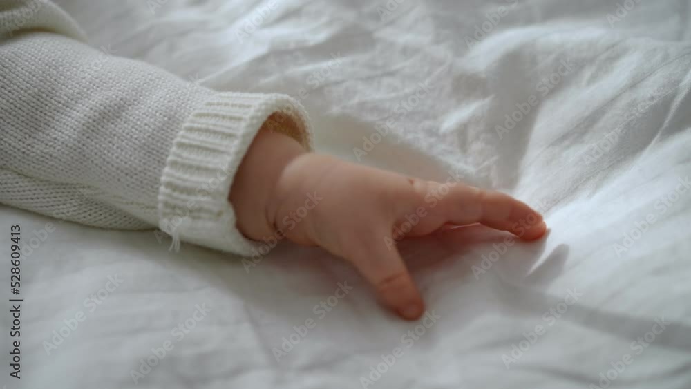 Close-up tiny palm of little baby on white soft comfortable bed. Hand of unrecognizable Caucasian infant toddler lying in cozy bedroom at home indoors. Tranquility and infancy concept Close-up tiny palm of little baby on white soft comfortable bed. Hand of unrecognizable Caucasian infant toddler lying in cozy bedroom at home indoors. Tranquility and infancy concept
