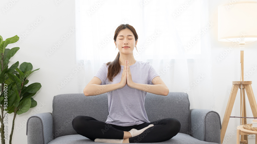 Beautiful young woman in sportswear is meditating or yoga and breathing on the sofa, Body and mind health care, Relaxation through meditation, Healthy exercise, Quiet living room. Beautiful young woman in sportswear is meditating or yoga and breathing on the sofa, Body and mind health care, Relaxation through meditation, Healthy exercise, Quiet living room.