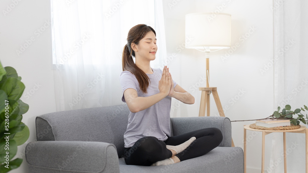 Beautiful young woman in sportswear is meditating or yoga and breathing on the sofa, Body and mind health care, Relaxation through meditation, Healthy exercise, Quiet living room. Beautiful young woman in sportswear is meditating or yoga and breathing on the sofa, Body and mind health care, Relaxation through meditation, Healthy exercise, Quiet living room.