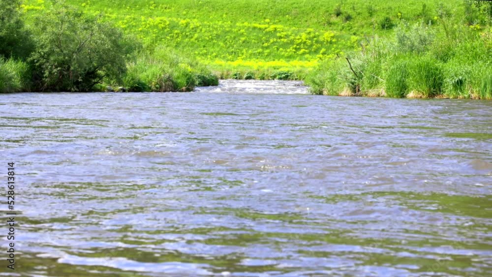 Close-up of the surface of a fast river, along the banks of which grow thorny shrubs. Fast flow of a cold mountain river with small waves Close-up of the surface of a fast river, along the banks of which grow thorny shrubs. Fast flow of a cold mountain river with small waves