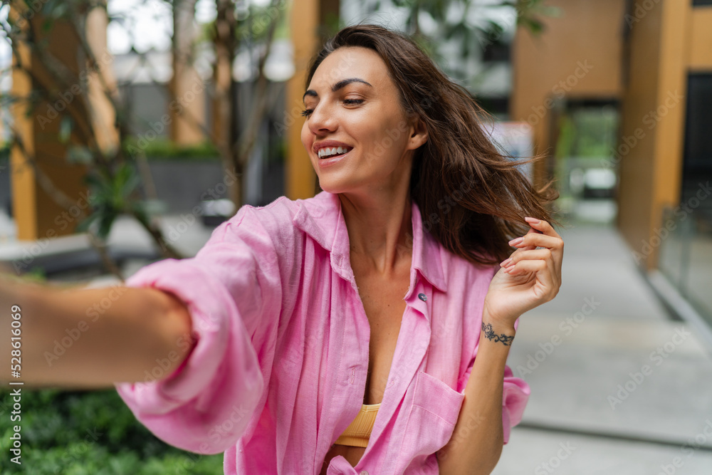 Outdoor lifestyle photo of  excited   european  woman in casual pink outfit making self portrait and  posing on the street.