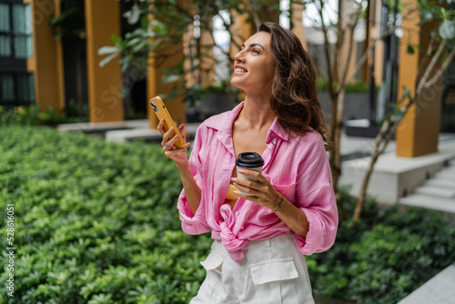Happy pretty woman in pink blouse  using mobyle phone and holding cup of coffee  doing online shopping. Summer style.