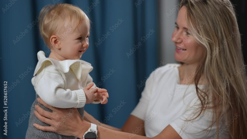 Joyful little baby girl smiling as woman talking to kid in slow motion standing indoors. Happy loving Caucasian mother and curios carefree toddler daughter chatting Joyful little baby girl smiling as woman talking to kid in slow motion standing indoors. Happy loving Caucasian mother and curios carefree toddler daughter chatting