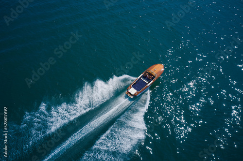 Classic wooden boat with motor moving on blue water aerial view. Italian wooden boat fast moving diagonal top view. An expensive wooden boat is an average movement on the water.