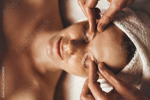 Caucasian freckled woman enjoying facial massage with closed eyes in spa salon. Beauty, spa, healthy lifestyle Facial massage at home. Massage the skin around