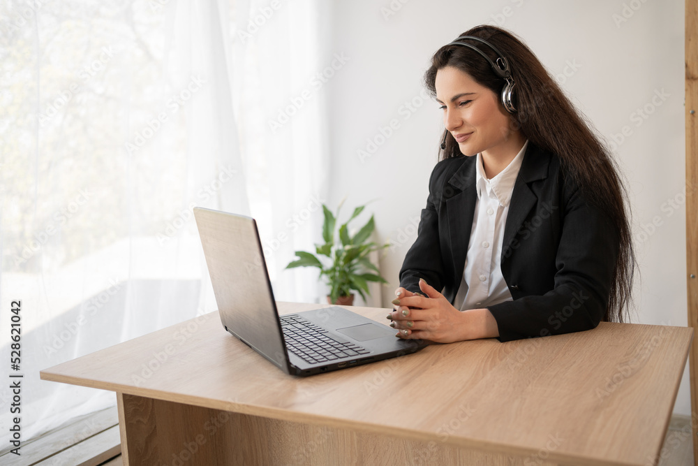 Latin woman in headphones working online using laptop in office, serious millennial female employee in headset consult client on Internet on computer, watching films online on her pc Latin woman in headphones working online using laptop in office, serious millennial female employee in headset consult client on Internet on computer, watching films online on her pc