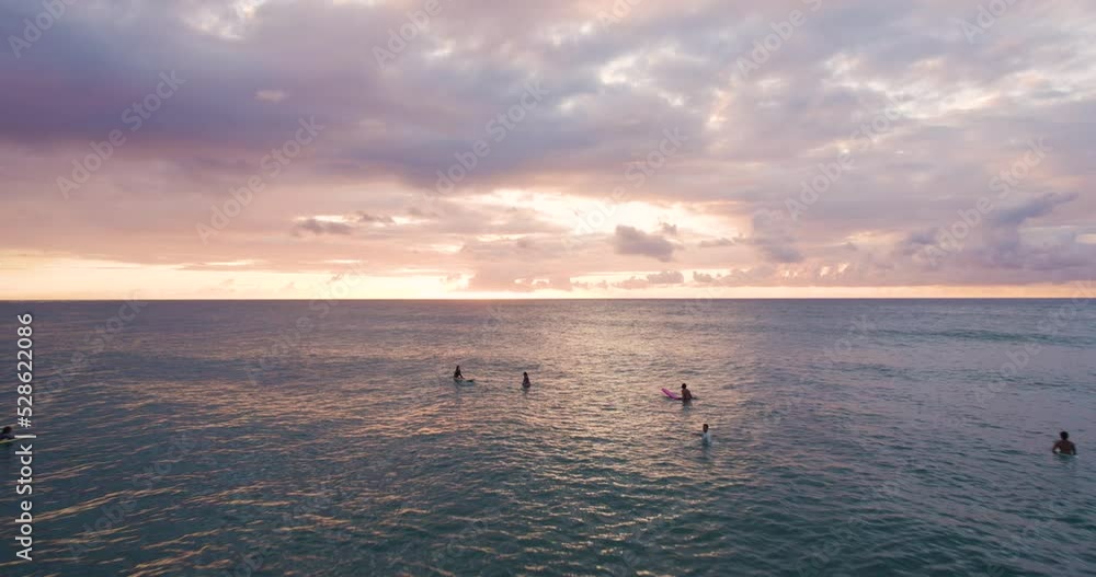 Surfers chilling in ocean waters in Oahu at sunset, Hawaii, flyover.