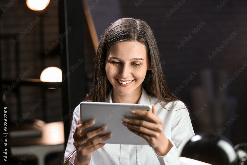 Smiling businesswoman working with tablet computer in office at night Smiling businesswoman working with tablet computer in office at night