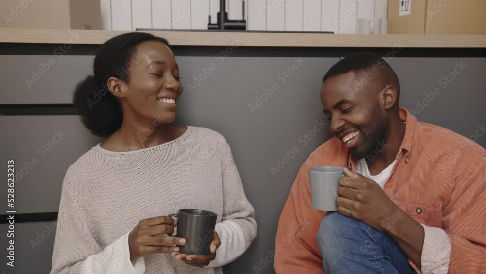 Close view of the happy african american couple sitting on the floor drinking hot tea or coffee and talking about their new home. New home and moving concept. Close view of the happy african american couple sitting on the floor drinking hot tea or coffee and talking about their new home. New home and moving concept.