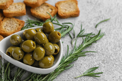 Bowl of tasty green olives and rosemary on light background, closeup