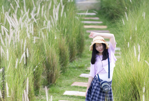 An Asian girl wearing brown hat in action with green grasses and white flowers in natural light.