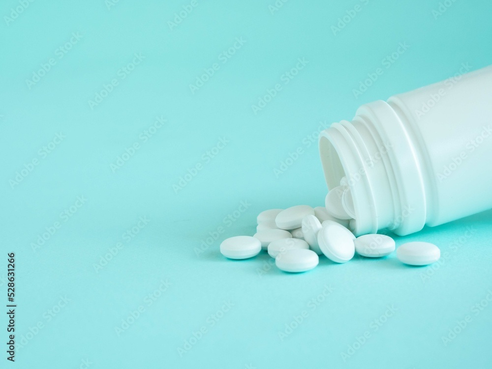 White tablets or multivitamins are poured out of a plastic jar on a blue one with a place for text White tablets or multivitamins are poured out of a plastic jar on a blue one with a place for text
